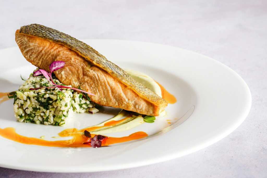 A beautifully plated salmon dish with quinoa, herbs, and a vibrant sauce, perfect for gourmet food lovers.